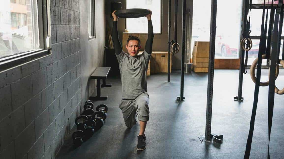 Man doing lunges gym with weight plate overhead
